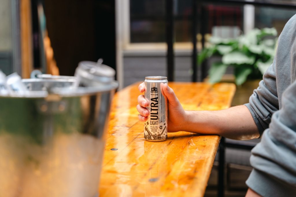 Person holding a can of Good Robot Ultra Light beer at a wooden table inside the brewery taproom.